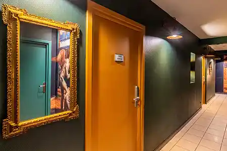long couloir coloré en vert avec des portes oranges et un miroir doré